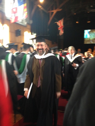 Man in cap and gown walking with diploma in hand