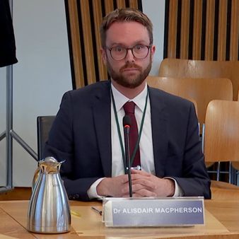 Dr Alisdair MacPherson sitting on a chair, looking towards the camera, while giving evidence to the Scottish Parliament’s Economy and Fair Work Committee
