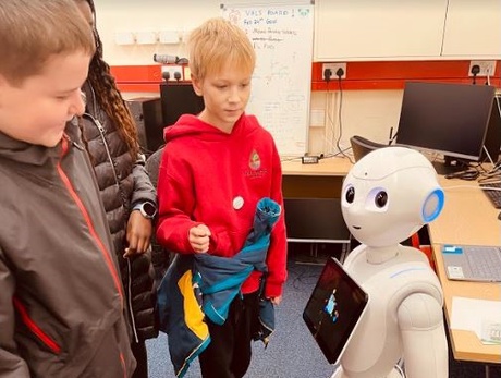 Two boys and a girl meeting a small white robot in the lab