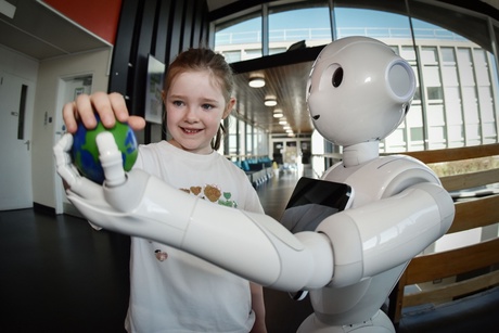 A young girl reaches for a globe held in the palm of a robot
