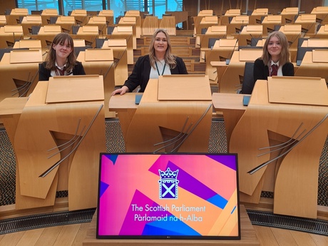 Katie, Karen Adam MSP and Chloe sitting in the Chamber at Holyrood