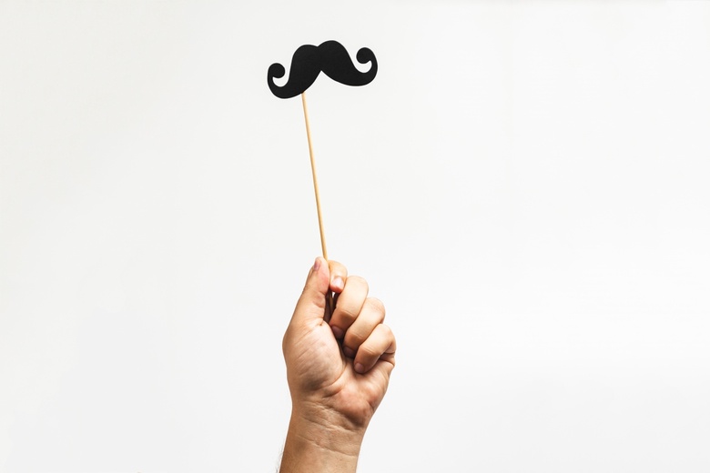 Hand holds up moustache prop on a stick