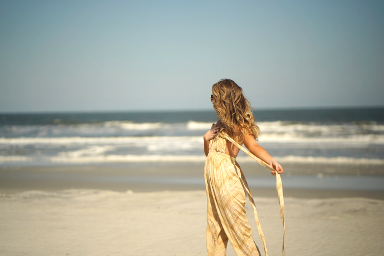 Woman with long hair stands on the beach facing out to sea