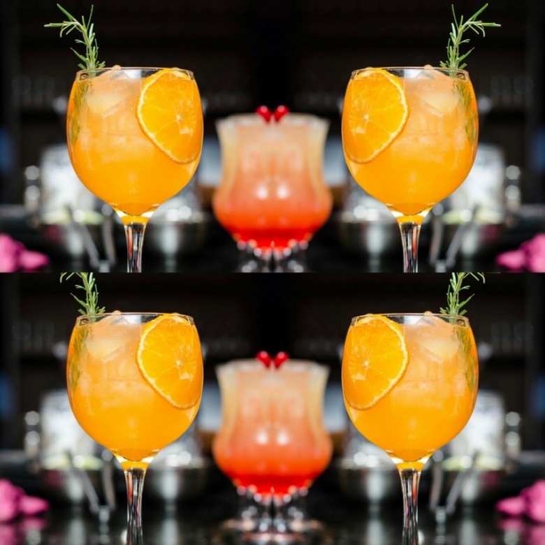Orange cocktail in a glass with a sprig of rosemary garnish