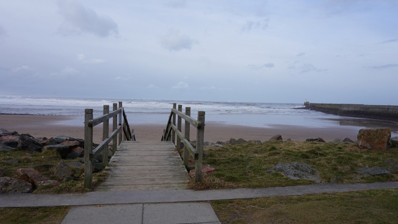A bridge leading down to Aberdeen beach. the backdrop is a blue sea with a dramatic grey sky.