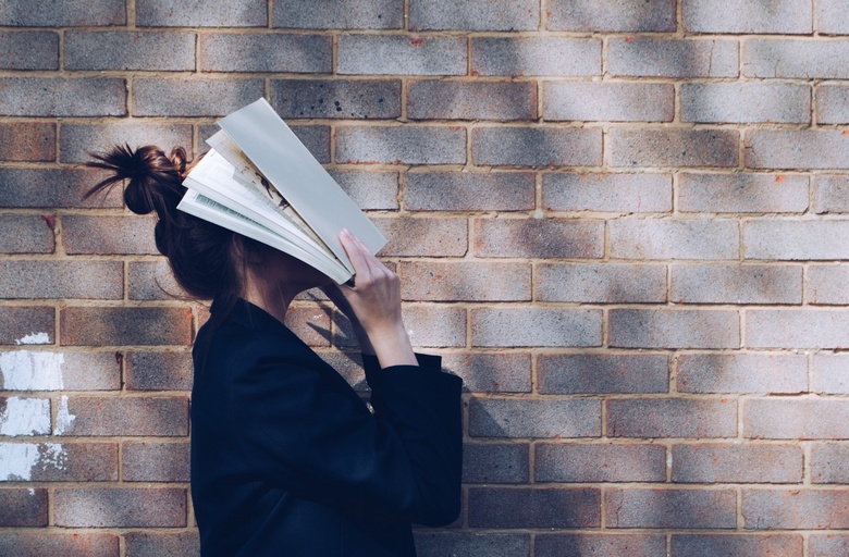 Image of student with head in a book against a brick wall