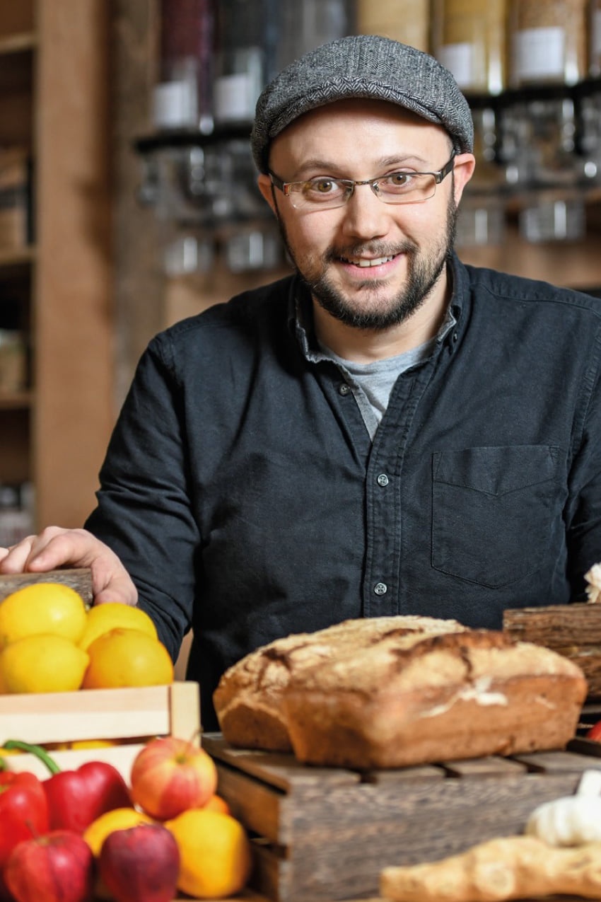 A man with glasses and a cap on sits in front of a table of freshly prepared food