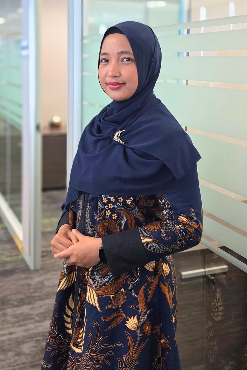 Woman in navy blue hijab standing in an office and smiling at camera