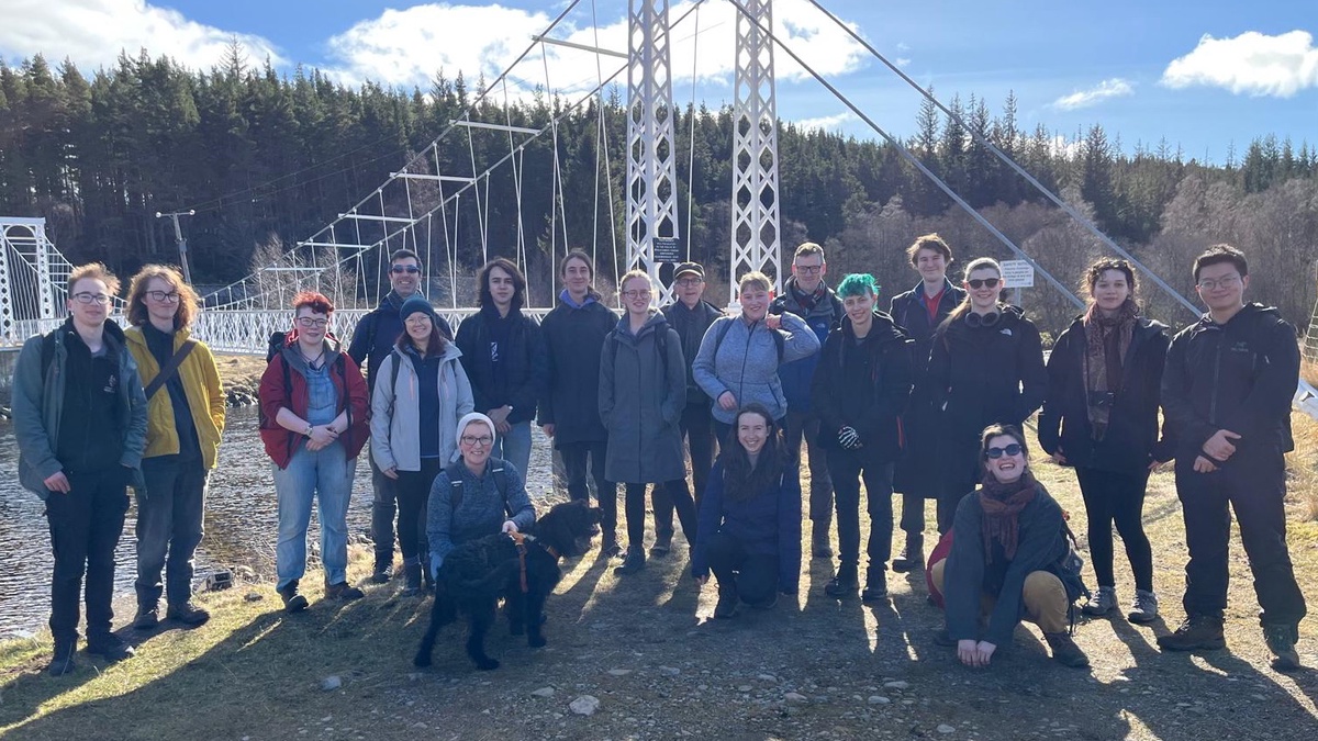 A group of Aberdeen Philosophy students and staff on a walk in the Cairngorms during the annual Philosophy Reading Party. They are standing in front of a bridge on a sunny day.