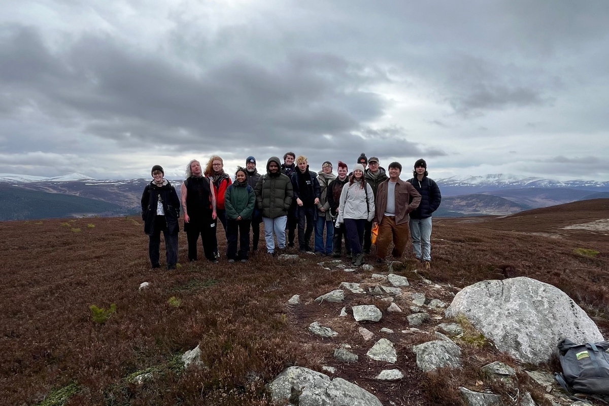 A group of Philosophy students at a peak in the Cairngorms. There are snow-capped mountains behind them.