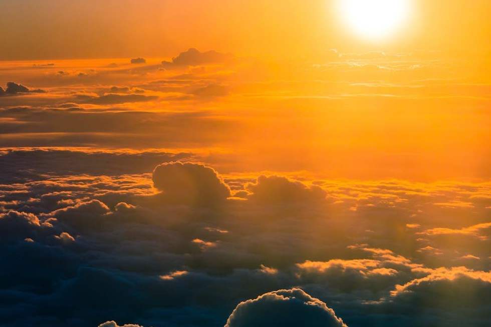 sun rising above a sea of dark clouds, casting a yellow orange glow on the sky