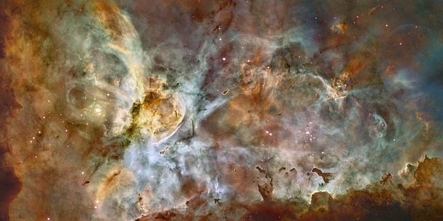 Carina nebula in the Milky Way galaxy. Clusters of stars are visible through golden, chocolate, and navy gas clouds