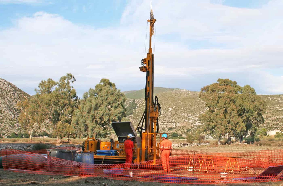 A huge yellow drill boring a large hole with two orange suited engineers overseeing the process