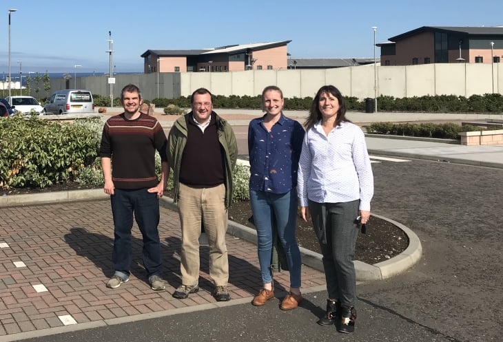four smiling people in a car park