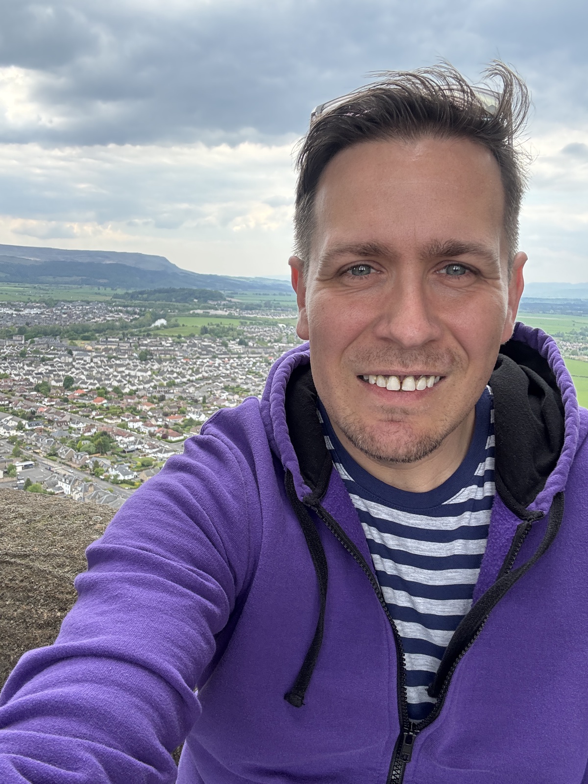 PGR student Adam Ferguson, in a purple jumper, on a hillside above a large town
