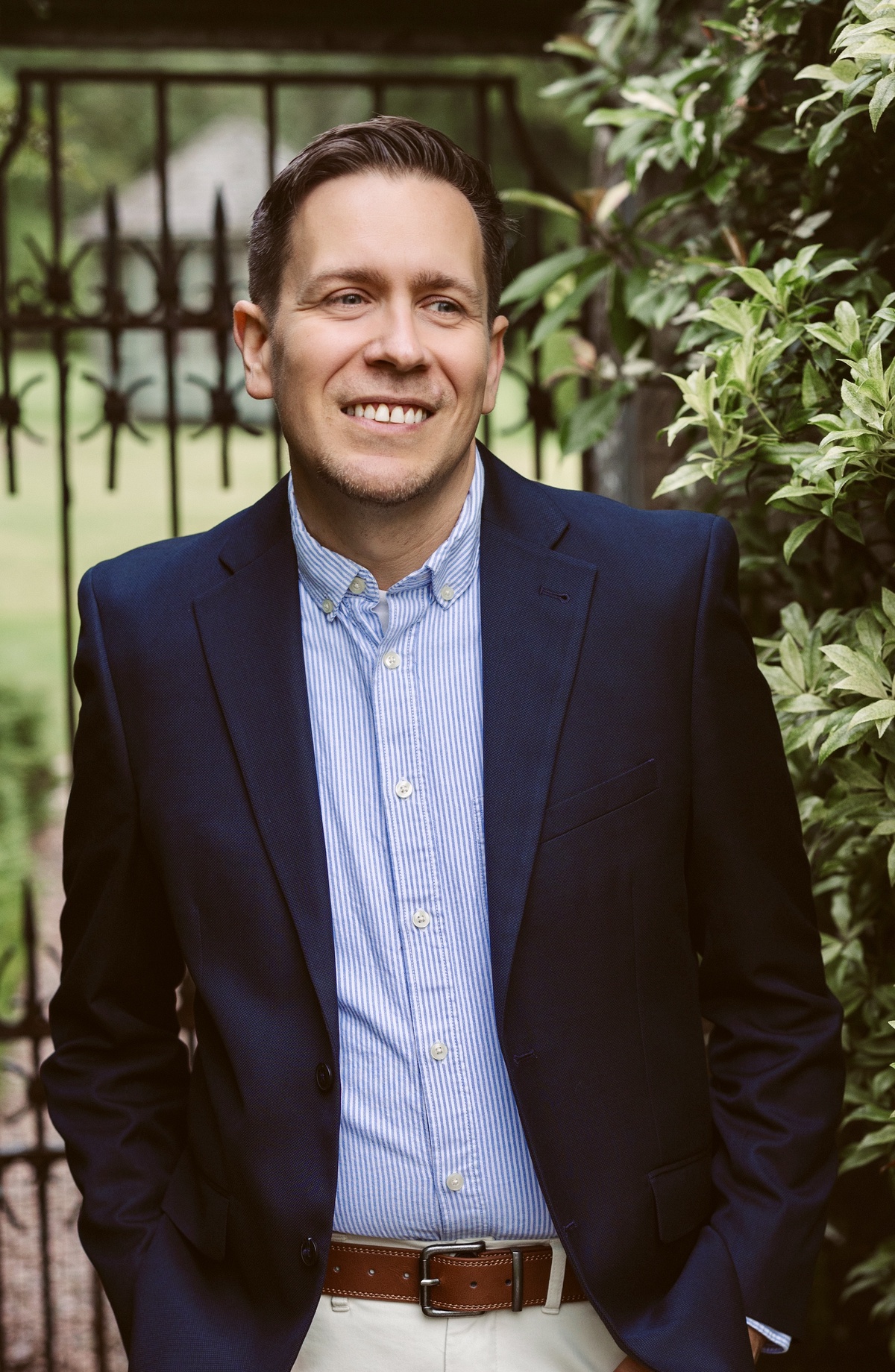 student Adam Ferguson, in a blazer and shirt, standing in front of an iron gate and a tree