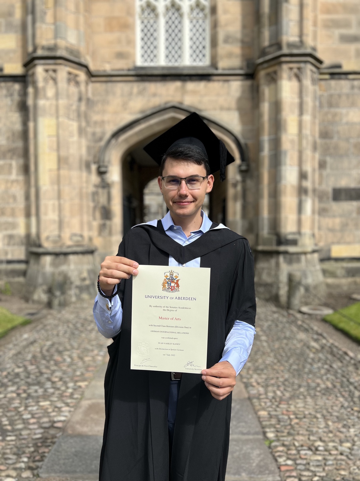 A male student wearing graduation robes and holding a degree certificate
