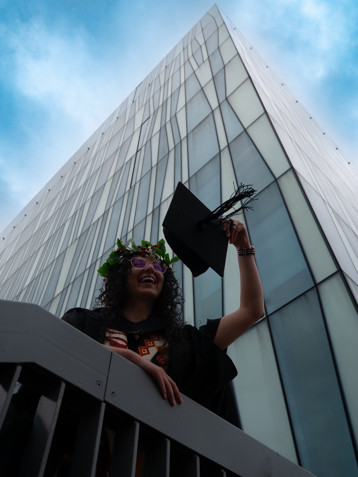 A female student wearing graduation robes below the Sir Duncan Rice Library