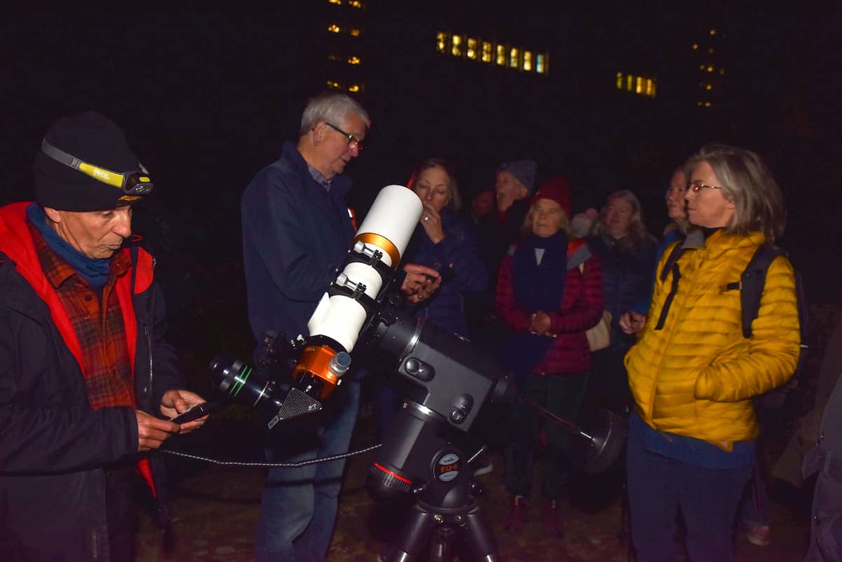 Visitors listen to an astronomer describing a telescope in the Rose Garden. It is dark and some visitors are wearing hats and gloves.