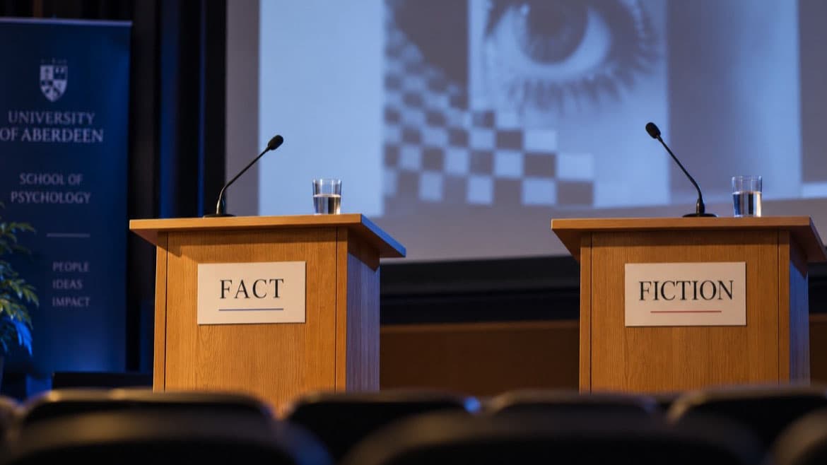 Stage in a lecture theatre with two podiums, one with a sign saying fact and the other with a sign saying fiction