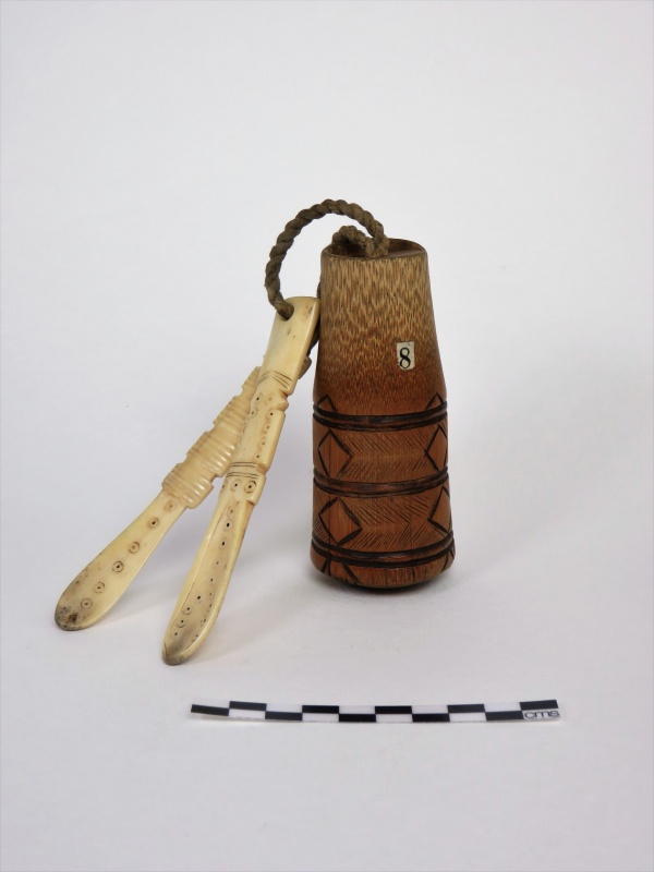 small wooden, cylindrical, snuff box with geometric pattern on the outside. Two ivory pieces attached by string as well. A sticker with the number eight is on the snuff box.