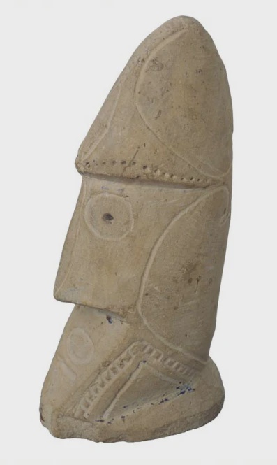 A stone carving resembling a face with geometric carvings on the side.