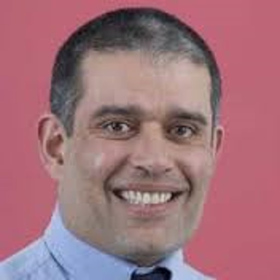 Photo of man smiling against pink background.