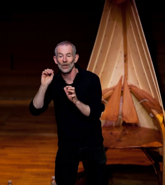 Man in back telling stories before sculpture of boat