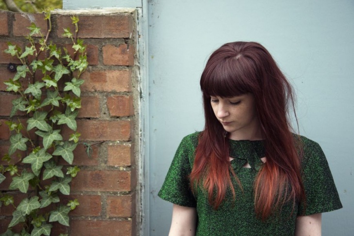 Woman in green standing in front of ivy-covered wall