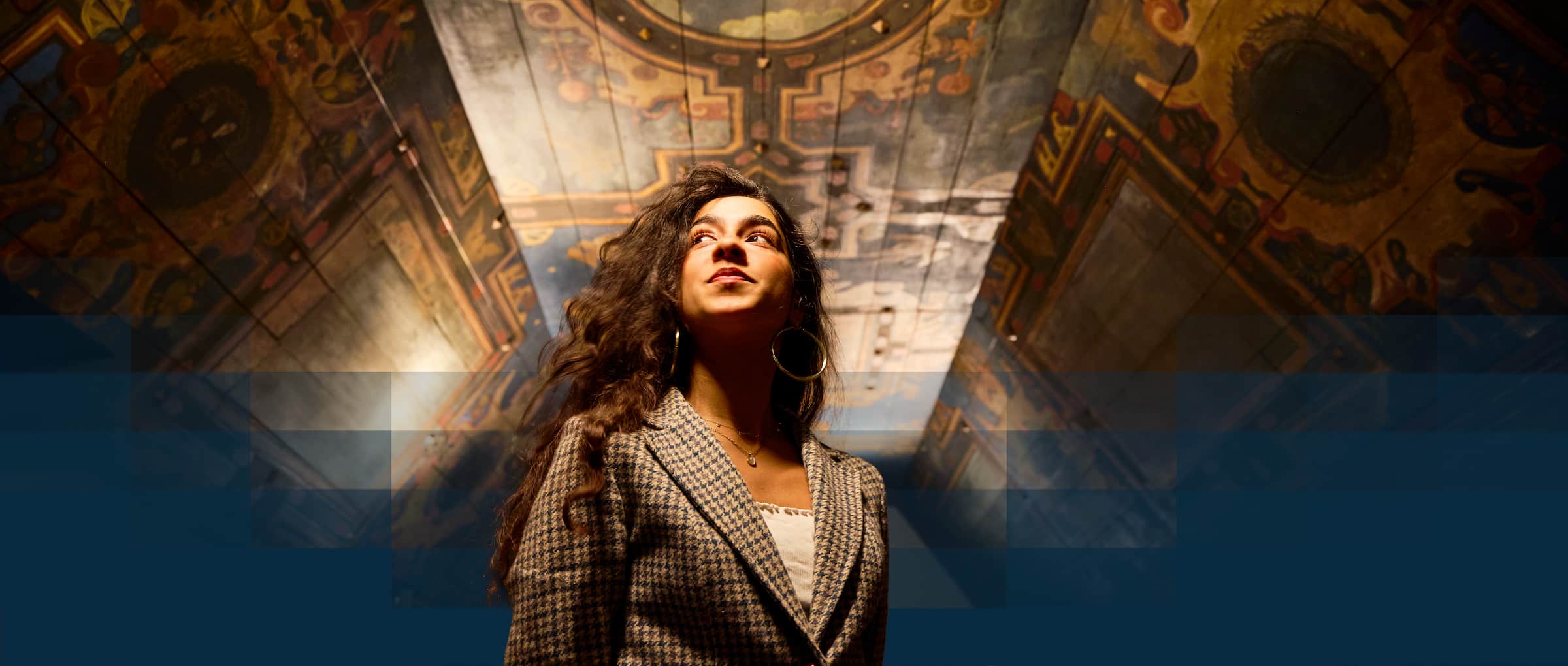 A female student in a medieval building looking at painted ceiling