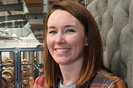 A woman with shoulder-length brown hair and a plaid shirt smiles at the camera