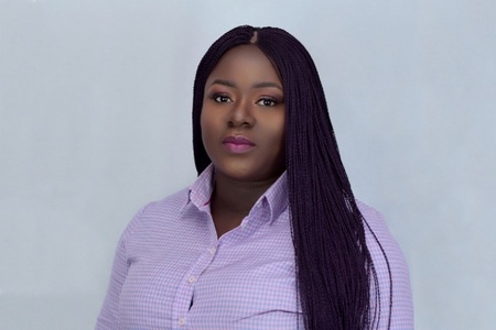 A woman with braided hair and a pink checked shirt looks toward the camera