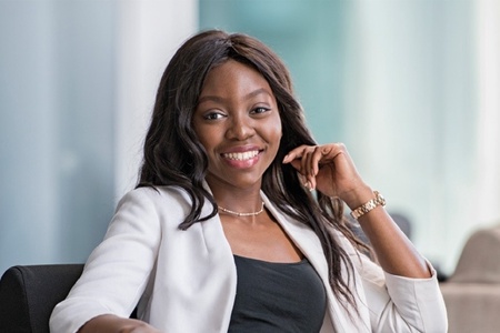 A woman with long dark hair wearing a light coloured blazer smiles at the camera