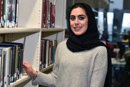 Female student wearing a hijab next to a bookshelf in the library