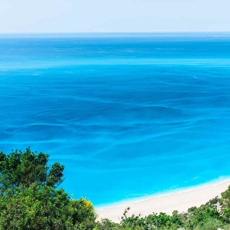 bright blue ocean and a shoreline with green trees and a sandy beach