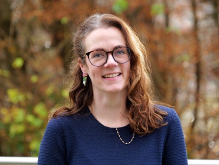 A photo of a lady's head and shoulders. Wearing a dark blue jumper and glasses.
