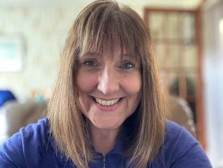 A photo of a lady's head and shoulders. Wearing a dark blue jumper. Mid-length hair and a fringe.
