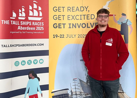 A man standing in front of a banner advertising the Tall Ships Race 2025