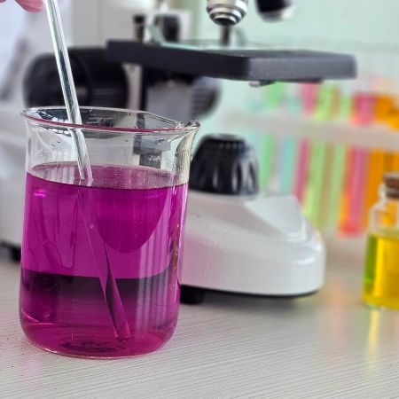 A beaker with bright purple liquid in front of a microscope