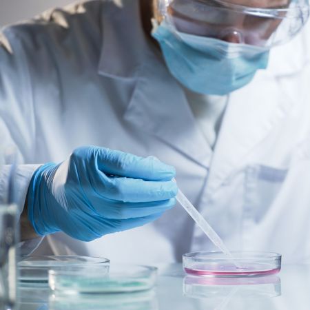 Someone wearing a lab coat testing a liquid in a petri dish