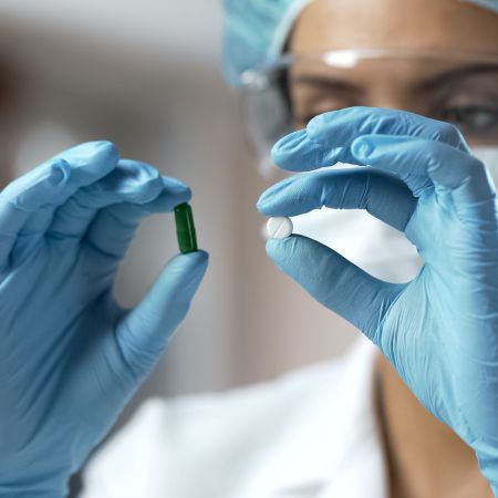A woman wearing blue gloves holding up two different pills