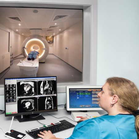 A woman looking at MRI scan photos with a person in an MRI scanner visible through window