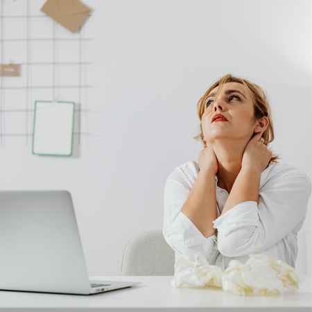 woman sitting at a desk with laptop holding neck looking stressed