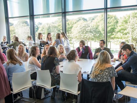 students sitting around tables in glass building