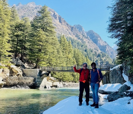 2 people standing next to a river with a mountain in the background