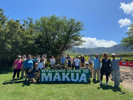 Group of people holding up a banner in front of Hawaiian landscape