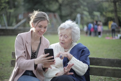 Younger woman showing older woman her mobile phone on a park bench
