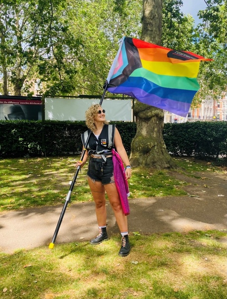 Nik Tait holding a pride flag in a park with tress in the background