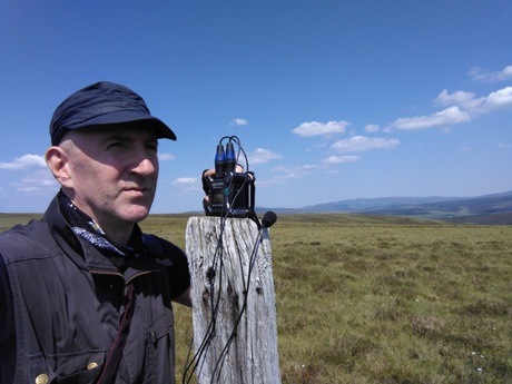 Profile of Dr Ali Rennie, recording sound in a field in the hills.