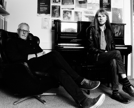 Pete and Joe Stollery, photographed in greyscale, sitting by a piano.
